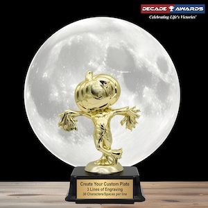 May include: A gold-colored trophy featuring a scarecrow figure with a pumpkin head, set against a large, bright moon. The trophy sits on a black base with a plate that reads "Create Your Custom Plate" and "3 Lines of Engraving". The Decade Awards logo is in the top right corner.