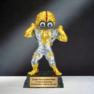 May include: A gold and silver trophy featuring a figure with a brain-shaped head and large eyes. The figure is tearing its shirt, revealing a silver torso and legs. The trophy sits on a black base with a gold plate that reads "Create Your Custom Plate".