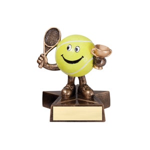 May include: A bronze tennis ball trophy with a smiling face, holding a tennis racket and a trophy cup. The trophy is standing on a star-shaped base with a blank plaque.