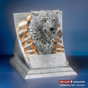 May include: Silver trophy with a wolf head sculpture and gold ribbons. The base has a rectangular space for engraving. The trophy reads "DECADE AWARDS Celebrating Life's Victories".