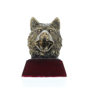May include: A bronze-colored wolf head trophy with an open mouth, mounted on a rectangular, dark red base. The wolf's fur is detailed, and the trophy has a metallic finish. The trophy is a decorative item.