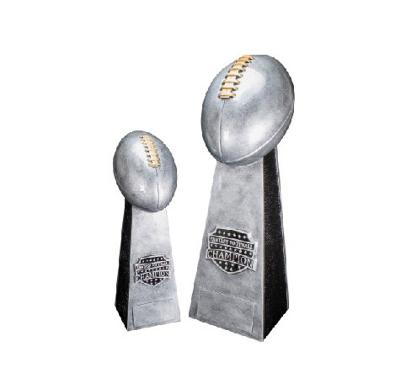 K&ouml;nnte beinhalten: Zwei silberne Fu&szlig;ball-Troph&auml;en mit schwarzen Sockeln. Die gr&ouml;&szlig;ere Troph&auml;e tr&auml;gt den Text "Fantasy Football Champion" auf dem Sockel.