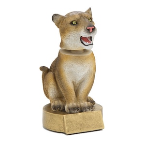 May include: A brown and tan cougar figurine with a gold base. The cougar is sitting with its mouth open and its eyes are yellow. The base has a blank plaque for engraving.
