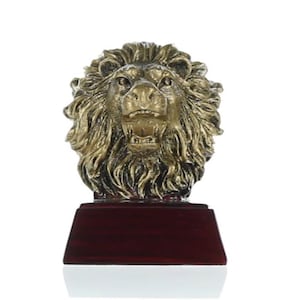 May include: A gold lion head trophy with a roaring expression. The lion head is mounted on a dark red wooden base.