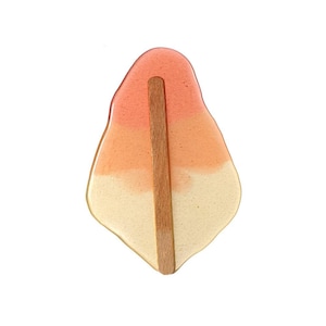 Könnte beinhalten: Ein rosa, orange und weißer Eis am Stiel mit einem Holzstiel. Das Eis am Stiel ist tropfenförmig und hat eine glatte, glänzende Oberfläche.