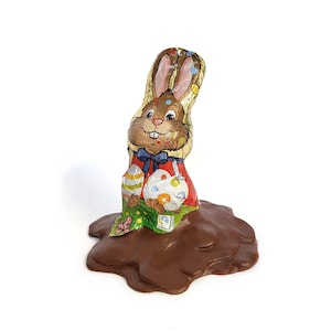 Puede incluir: Un conejito de chocolate con diseños coloridos de huevos de Pascua está atascado en un charco de chocolate derretido.