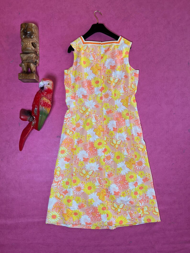 May include: A sleeveless dress with a floral print in shades of pink, yellow, and white. The dress has a scoop neck and a back zip fastening.