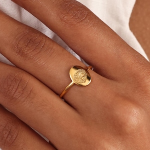 May include: A gold ring with a round, textured, gold disc. The disc has a design on it.