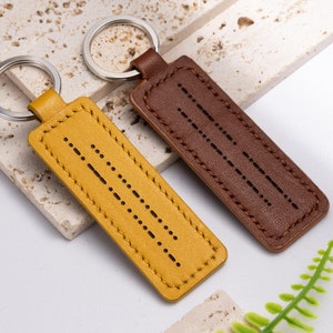 May include: Two leather keychains with metal rings. One keychain is brown with a pattern of dots and the other is yellow with a pattern of dots.