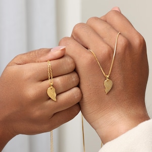 May include: Two gold-toned necklaces, each featuring a pendant shaped like one half of a heart. The surface of each pendant is textured with a detailed fingerprint pattern. The pendants hang from delicate gold-toned box chains.