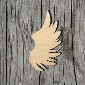 May include: A single wooden angel wing cutout, with a light brown color and a detailed design. The wing is against a rustic wooden background.