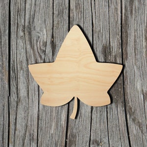 May include: A wooden cutout of an ivy leaf, with a natural wood finish. The leaf is isolated against a rustic wood background.