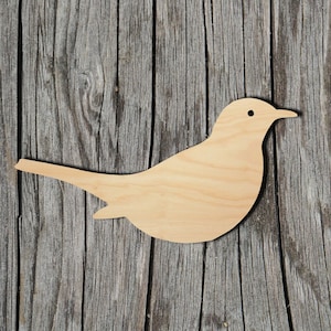 May include: A wooden cutout of a bird in a light brown color. The bird is facing right and has a simple design. The cutout is on a weathered wooden background.