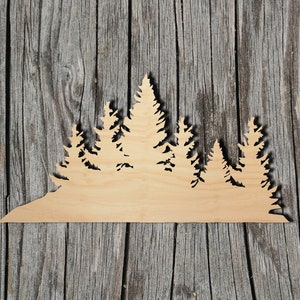May include: A wooden cutout of a forest silhouette with multiple pine trees. The cutout is made of light brown wood and has a natural wood grain.