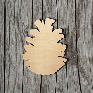 May include: A wooden cutout of a pine cone, with a natural wood finish. The cutout is on a gray wood background.