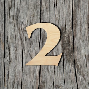 May include: A wooden number two cutout, painted in a light brown color, is placed on a weathered gray wooden surface.