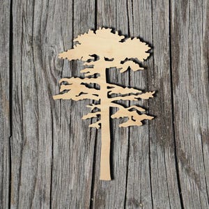 May include: A laser-cut wooden tree silhouette with a detailed design. The tree is light brown and set against a weathered, gray wooden background. The tree features a full crown and detailed branches.