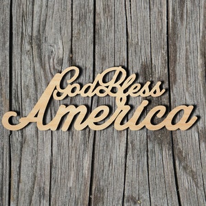 May include: Wooden sign with the text "God Bless America" in a cursive font. The sign is light brown and has a rustic look.