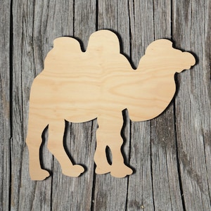May include: A wooden cutout of a camel in a standing position. The camel is facing right and has a hump on its back. The cutout is made of light brown wood and has a smooth surface.
