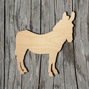 May include: A wooden donkey cutout in a light tan color. The donkey is standing in profile, with its ears and tail visible. The cutout is placed on a weathered, gray wooden surface.