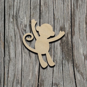 May include: A wooden cutout of a monkey with its arms raised and a curled tail. The cutout is a light brown color and is placed on a weathered wooden background.