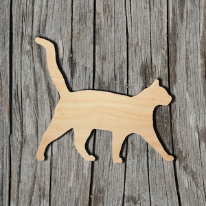 May include: A flat, light-colored wooden cutout in the shape of a walking cat with its tail held high. The silhouette features a smooth, natural wood grain texture and clearly defined edges, depicting the feline in a side profile walking pose.