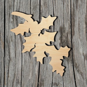 May include: A light-colored, flat wooden cutout shaped like a cluster of holly leaves and berries. The object features a smooth, natural wood grain finish with distinct, jagged leaf edges and rounded berry shapes integrated into the design.