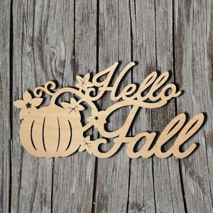 May include: Wooden cutout sign with the words "Hello Fall" in cursive script, accompanied by a pumpkin and leaf design. The sign is made of light-colored wood and is set against a weathered wood background.