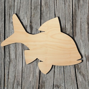 May include: A wooden cutout of a fish shape, painted in a natural wood color. The fish is facing right and has a slightly curved body. The cutout is on a wooden background.