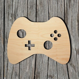 May include: A wooden cutout of a video game controller. The controller is light brown and has a simple design with four buttons, a directional pad, and two trigger buttons.