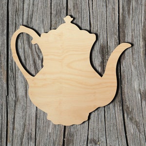 May include: A wooden cutout of a teapot in the shape of a traditional tea pot. The cutout is made of light brown wood and has a smooth surface.