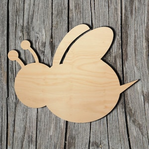 May include: A wooden cutout of a bee in a simple, cartoon-like style. The bee is light brown and has a rounded body and two small antennae.
