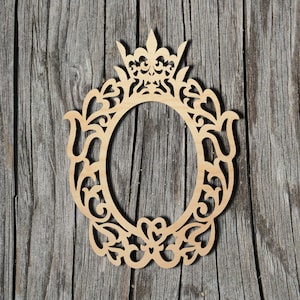 May include: A wooden cutout of a decorative frame with a crown at the top and intricate floral designs. The frame is oval shaped and has a blank space in the center.