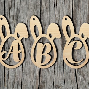 May include: Three wooden Easter bunny ornaments with the letters A, B, and C cut out. The ornaments are painted in a natural wood color.
