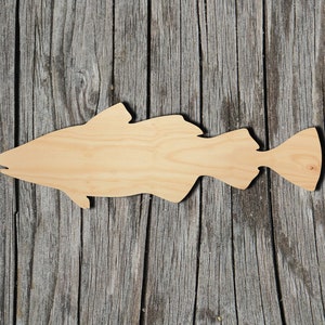 May include: A wooden cutout of a fish, painted in a natural wood color. The fish is facing to the right and has a slightly curved body. The cutout is placed on a weathered wooden background.
