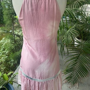 May include: A sleeveless pink dress with a subtle white tie-dye pattern, featuring a metallic silver snakeskin-textured trim around the neckline and a matching horizontal band above the pleated hemline, displayed on a mannequin.