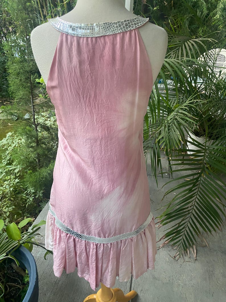 May include: A sleeveless pink dress with a subtle white tie-dye pattern, featuring a metallic silver snakeskin-textured trim around the neckline and a matching horizontal band above the pleated hemline, displayed on a mannequin.