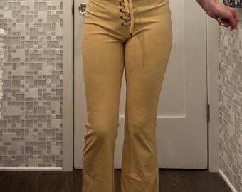 May include: Mustard-colored flared pants with a high waist and a lace-up front. The pants are made of a soft material and have a subtle sheen. The pants are paired with a patterned top.