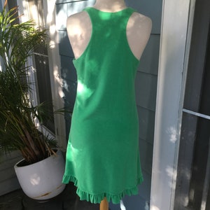 May include: A bright green, sleeveless dress with a racerback design. The dress has a ruffled hem and is displayed on a mannequin. The dress is made of a soft, textured fabric.