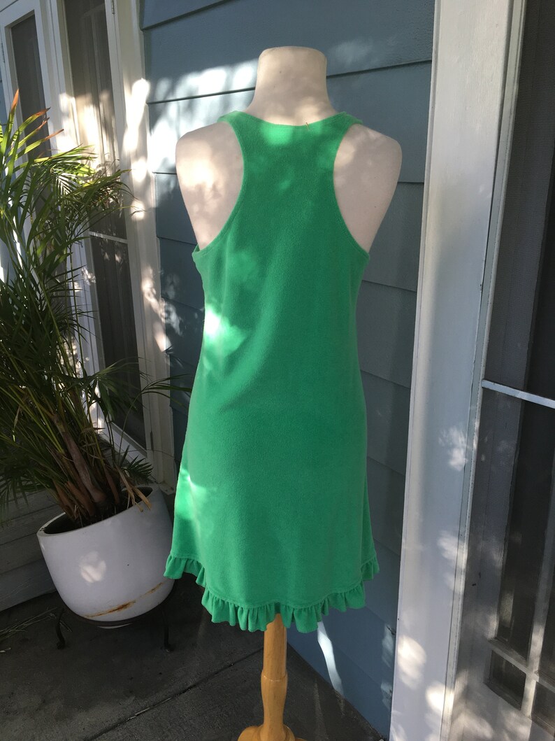 May include: A bright green, sleeveless dress with a racerback design. The dress has a ruffled hem and is displayed on a mannequin. The dress is made of a soft, textured fabric.