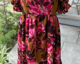 May include: A midi-length dress with a square neckline and puff sleeves. The dress is made of a lightweight fabric with a floral print in shades of pink, brown, and green.