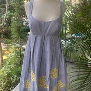 May include: A sleeveless knee-length dress featuring a blue and white pinstripe pattern, a scoop neckline, and a pleated skirt. The lower portion of the dress is decorated with embroidered yellow floral motifs arranged in a scattered pattern.