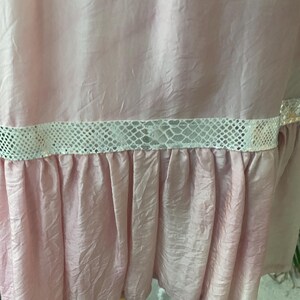 May include: A light pink garment with a crinkled texture featuring a horizontal band of white snakeskin-patterned trim above a gathered ruffle hem. The fabric has a subtle sheen and the design includes a distinct horizontal seam detail.