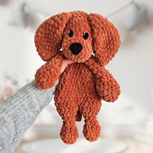 May include: A crocheted plush toy dog in a brown color. The dog has a black nose and eyes.