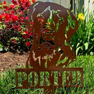 May include: A brown metal silhouette of a dog's head with the name "PORTER" written below it. The silhouette is standing in a grassy area.