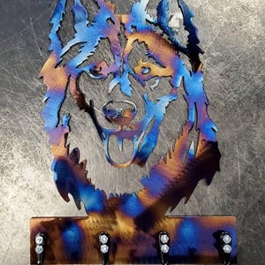 May include: A metal wall-mounted key holder featuring a stylized husky dog head. The metal has a heat-treated finish with blue, bronze, and gold hues. The key holder has three black hooks for hanging keys.