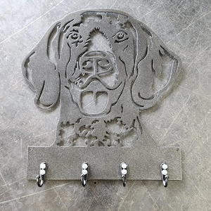 May include: A metal key holder featuring a dog's head silhouette. The gray key holder has a rectangular base with four hooks. The dog's face is detailed with cut-out features, including eyes, nose, and mouth.
