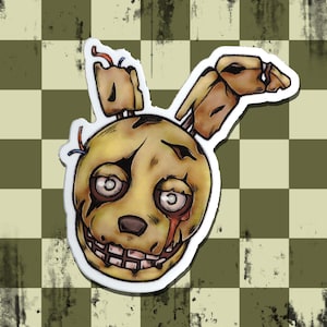 May include: A die-cut sticker featuring a stylized, weathered yellow rabbit head with a damaged ear, large circular eyes, a dark nose, and a wide, toothy grin. The character has visible cracks and red markings, with small blue and red wires protruding from the top of the head, rendered in a comic book illustration style with bold black outlines.