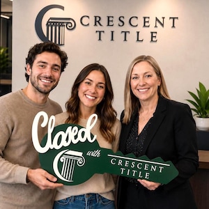 May include: A large, dark green, key-shaped sign with white lettering that reads Closed with Crescent Title, featuring a white pillar logo. The sign is held by three people standing in front of a wall with the Crescent Title logo and text.