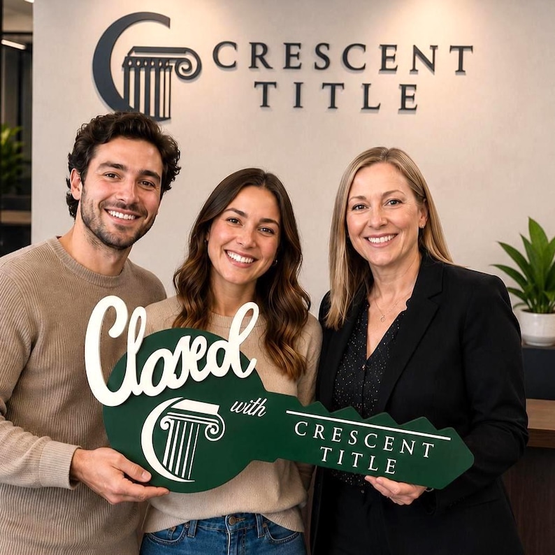 May include: A large, dark green, key-shaped sign with white lettering that reads Closed with Crescent Title, featuring a white pillar logo. The sign is held by three people standing in front of a wall with the Crescent Title logo and text.